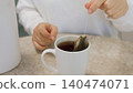 Person steeping tea bag in hot water inside white mug 140474071