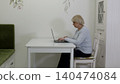 Senior woman typing on laptop at white desk in bright home office 140474084