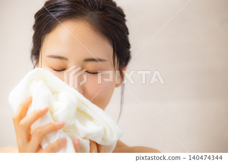 A woman sniffing a towel in the bathroom. 140474344