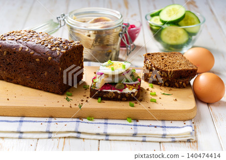 traditional scandinavian sandwich smorrebrod with herring ,red onion, boiling egg, and rye bread on cutting board, selective focus. traditional scandinavian sandwich smorrebrod with herring ,red onion, boiling egg, and rye bread on cutting board, selective focus. 140474414