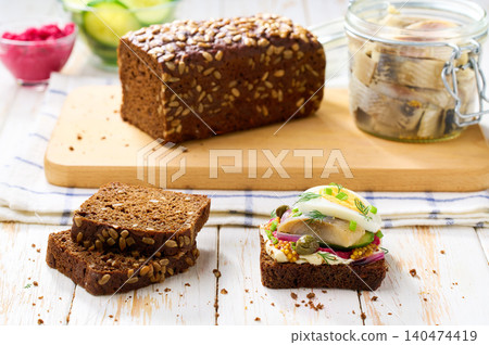 Black rye bread with butter, herring fish, boiled eggs, capers and red onion on a table. Traditional Danish open sandwich smorrebrod. Black rye bread with butter, herring fish, boiled eggs, capers and red onion on a table. Traditional Danish open sandwich smorrebrod. 140474419