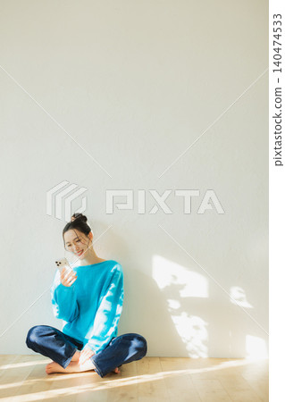 年輕女子坐在地板上看著智慧型手機 年輕女子坐在地板上看著智慧型手機 140474533