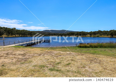 View of Dumaresq Dam and jetty in Armidale, New South Wales, Australia under clear blue sky. Scenic waterscape showing calm freshwater environment in regional New England area. View of Dumaresq Dam and jetty in Armidale, New South Wales, Australia under clear blue sky. Scenic waterscape showing calm freshwater environment in regional New England area. 140474619