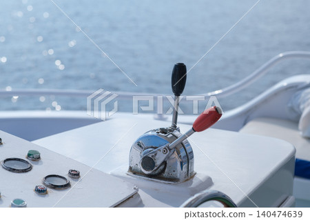 Boat throttle control lever features chrome finish and gauges on dashboard, with glistening water surface visible in the background under sunlight Boat throttle control lever features chrome finish and gauges on dashboard, with glistening water surface visible in the background under sunlight 140474639