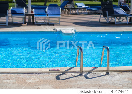 Swimming pool features clear blue water and a stainless steel ladder, surrounded by lounge chairs on a sunny outdoor deck area Swimming pool features clear blue water and a stainless steel ladder, surrounded by lounge chairs on a sunny outdoor deck area 140474645
