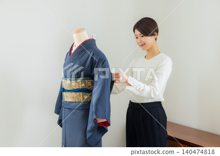 A woman practicing how to put on a kimono on a mannequin. A woman practicing how to put on a kimono on a mannequin. 140474818
