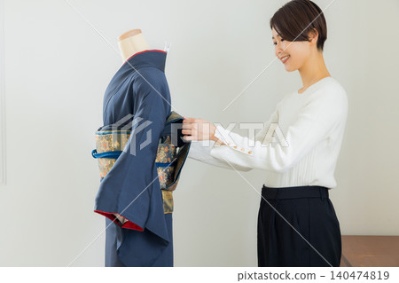 A woman practicing how to put on a kimono on a mannequin. A woman practicing how to put on a kimono on a mannequin. 140474819