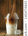 Iced latte coffee drink featuring distinct layers of espresso and milk with ice cubes in clear plastic cup on wooden surface 140474845