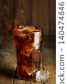 Refreshing sparkling cola with melting ice cubes in a glass creating condensation on rustic wooden background 140474846