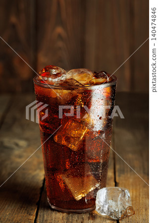 Refreshing sparkling cola with melting ice cubes in a glass creating condensation on rustic wooden background Refreshing sparkling cola with melting ice cubes in a glass creating condensation on rustic wooden background 140474846