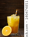 Fresh squeezed orange juice with ice and striped straw beside sliced ripe orange on dark wood 140474851
