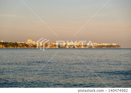 Overlooking tranquil waters, a coastal city skyline glows in the warm light of sunset, showcasing buildings against a clear sky. Overlooking tranquil waters, a coastal city skyline glows in the warm light of sunset, showcasing buildings against a clear sky. 140474982