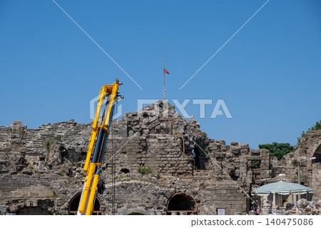 Cranes work on the restoration of ancient stone ruins while a flag flies above a historic site on a sunny day with a clear blue sky Cranes work on the restoration of ancient stone ruins while a flag flies above a historic site on a sunny day with a clear blue sky 140475086