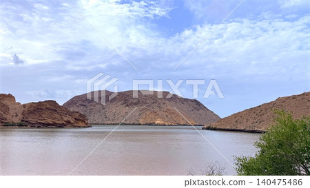 Calm desert reservoir with distant rocky hills under a partly cloudy sky Calm desert reservoir with distant rocky hills under a partly cloudy sky 140475486