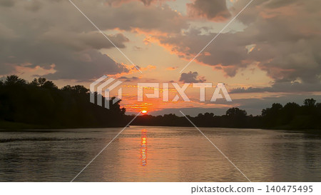 A picturesque sunset over the river with reflections of clouds and silhouettes of trees A picturesque sunset over the river with reflections of clouds and silhouettes of trees 140475495