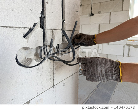 electrical wiring in a new building. A male electrician installs an electrical cable into the wall of a new building. Construction and repair electrical wiring in a new building. A male electrician installs an electrical cable into the wall of a new building. Construction and repair 140476178