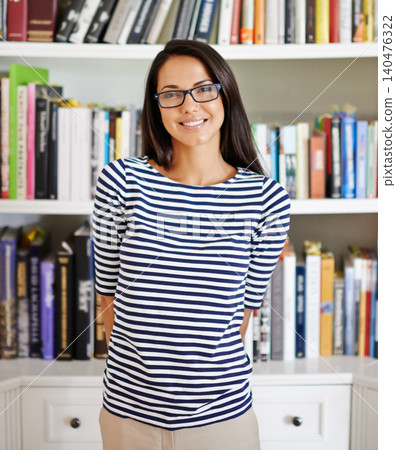 Woman, portrait and happy by bookshelf in house with books for reading, learning and knowledge in living room. Person, face and confidence by home library with magazine, journal and study collection 140476322