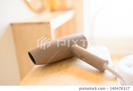 A beige hair dryer placed on a wooden stand. A beige hair dryer placed on a wooden stand. 140476327