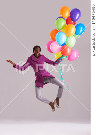 Balloon, jump and portrait of happy black woman in studio for birthday, celebration and present. Fashion, excited and isolated person with inflatable for party, gift and surprise on gray background Balloon, jump and portrait of happy black woman in studio for birthday, celebration and present. Fashion, excited and isolated person with inflatable for party, gift and surprise on gray background 140476490