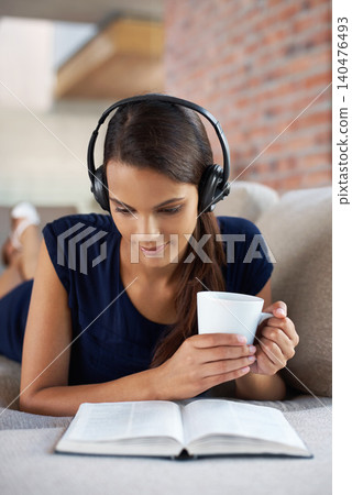 Music, book and woman relax with coffee in home on holiday or vacation and headphones streaming audio. Girl, reading and listening to sound on sofa in apartment on weekend with green tea or drink 140476493