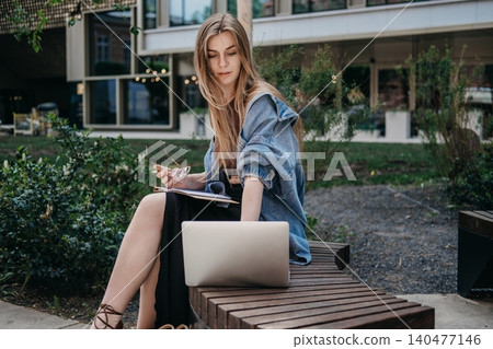 Woman holds glasses while looking down towards laptop on wooden bench in outdoor park. Women in technology, self-employed female Empowered woman outdoor, remote work productivity, modern career paths. Woman holds glasses while looking down towards laptop on wooden bench in outdoor park. Women in technology, self-employed female Empowered woman outdoor, remote work productivity, modern career paths. 140477146