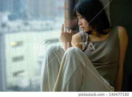 雨中,一個女人坐在窗邊。 雨中,一個女人坐在窗邊。 140477180