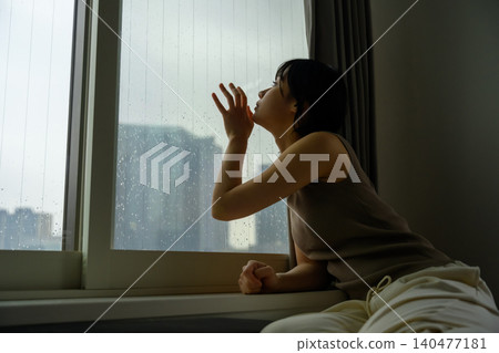 A woman watching the rain from a window. A woman watching the rain from a window. 140477181