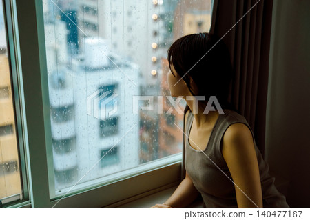 A woman watching the rain from a window. A woman watching the rain from a window. 140477187