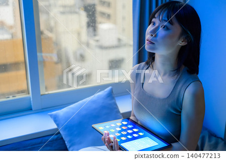 A woman sitting by the window with a tablet in her hand. A woman sitting by the window with a tablet in her hand. 140477213