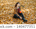 Woman sits on ground covered with autumn leaves holding beverage container. Mindful lunch break, work life balance outdoor, mental health relaxation. 140477351