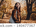 Woman stands in park holding canvas tote bag filled with autumn leaves. Sustainable autumn fashion, zero waste fall decor, eco conscious living. 140477367