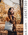 Woman stands in park with tote bag containing autumn leaves. Zero waste lifestyle, eco friendly shopper bag, sustainable consumer habits. 140477369