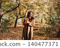Woman stands in park holding yellow maple leaf looking sideways. Emotional self regulation, mental clarity practice, finding inner peace. 140477371