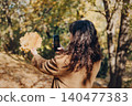 Person takes smartphone picture of yellow autumn leaves while smiling in park. Social media influencer lifestyle, autumn blogging content, lifestyle vlogger in park. 140477383
