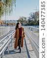 Woman walks on modern pedestrian bridge walkway while looking sideways. Walkable city infrastructure, modern urban pedestrian zone, navigating city architecture, accessible urban environment. 140477385