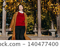 Woman smiles while walking outdoors near trees with autumn foliage. Expressing pure happiness, positive mental health, mindfulness in daily life, optimism and wellbeing. 140477400