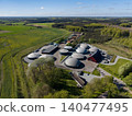 Drone view looking across a biogas energy facility toward vast green and yellow agricultural fields in Denmark 140477495