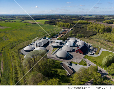 Drone view looking across a biogas energy facility toward vast green and yellow agricultural fields in Denmark 140477495