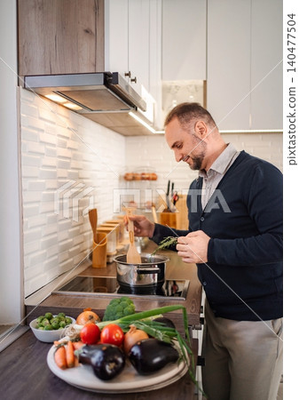 Adult man cooking healthy meal with fresh vegetables in kitchen Adult man cooking healthy meal with fresh vegetables in kitchen 140477504