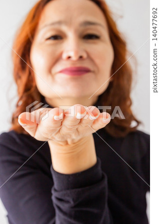 Woman blowing a kiss with her hand toward camera. Female showing gesture of affection or greeting. Romantic emotion and positive expression for kindness, love, connection, and friendship. 140477692