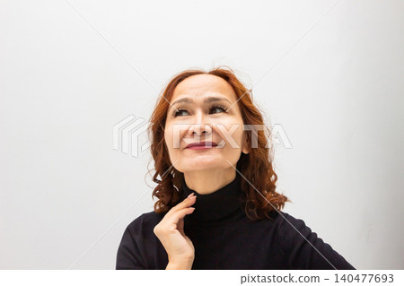 Woman with red hair looking up with a thoughtful smile. Portrait of a happy lady contemplating future dreams. Positive expression and emotion of a Woman expressing hope and inspiration. Woman with red hair looking up with a thoughtful smile. Portrait of a happy lady contemplating future dreams. Positive expression and emotion of a Woman expressing hope and inspiration. 140477693