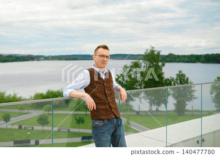 Stylish middle-aged man stands on balcony of observation desk near lake in city park Stylish middle-aged man stands on balcony of observation desk near lake in city park 140477780