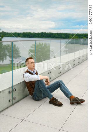 Relaxed middle-aged man sitting by lake on modern terrace during cloudy weather 140477785