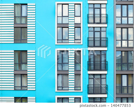 A vibrant blue facade of a contemporary multi-story residential building showcasing a grid of windows and balconies 140477853