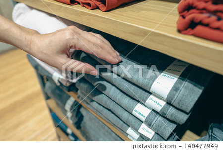 Woman shopping jeans in clothing store. Woman choosing clothes. Jeans on wooden shelves in clothing store. Fashion retail shop inside shopping mall. Black jeans on wooden shelves in a clothes shop. Woman shopping jeans in clothing store. Woman choosing clothes. Jeans on wooden shelves in clothing store. Fashion retail shop inside shopping mall. Black jeans on wooden shelves in a clothes shop. 140477949