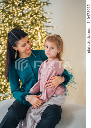 Mother and daughter sit together near a decorated tree Mother and daughter sit together near a decorated tree 140478015
