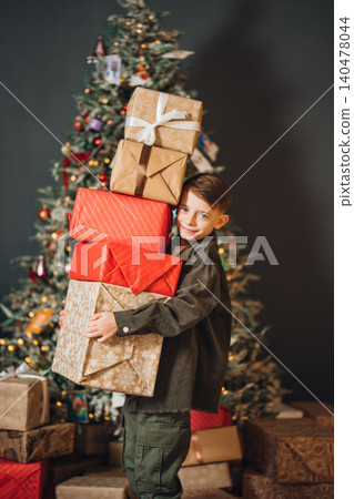 Child carries wrapped gifts in front of Christmas tree in indoor setting Child carries wrapped gifts in front of Christmas tree in indoor setting 140478044
