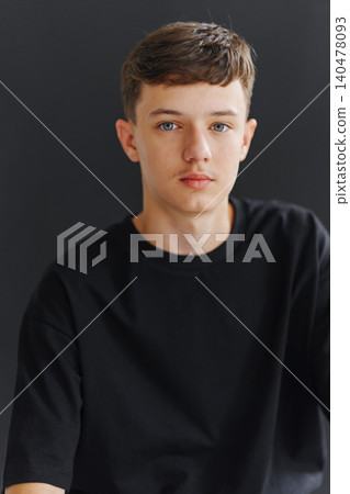 Young person sitting in front of dark background with calm expression Young person sitting in front of dark background with calm expression 140478093