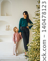 Woman and girl stand by Christmas tree in modern indoor setting 140478123