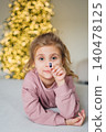 Child holds a small item in front of a lit Christmas tree 140478125